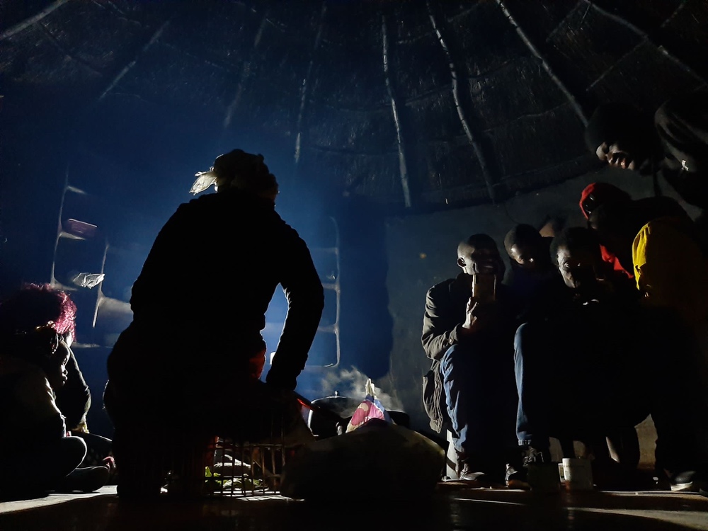 People gathered in a thatched hut at night, lit by a central light